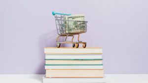 A small cart toy with money inside on top of a pile of books
