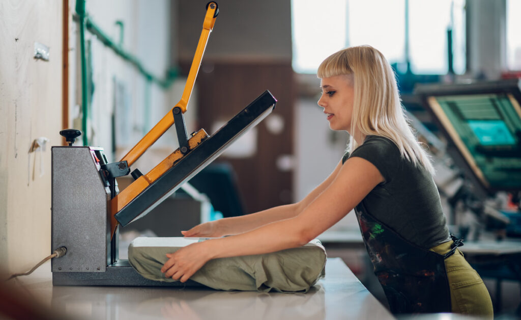 A woman printing a design onto a blank t-shirt