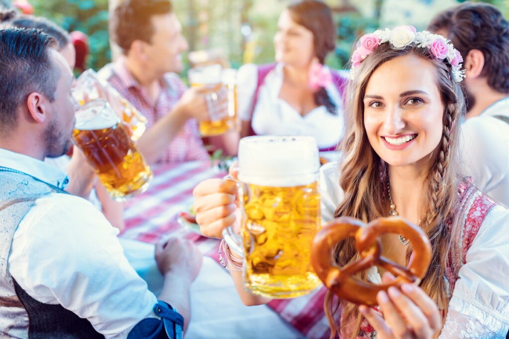 A woman in a dirndl drinks a large beer at an oktoberfest party
